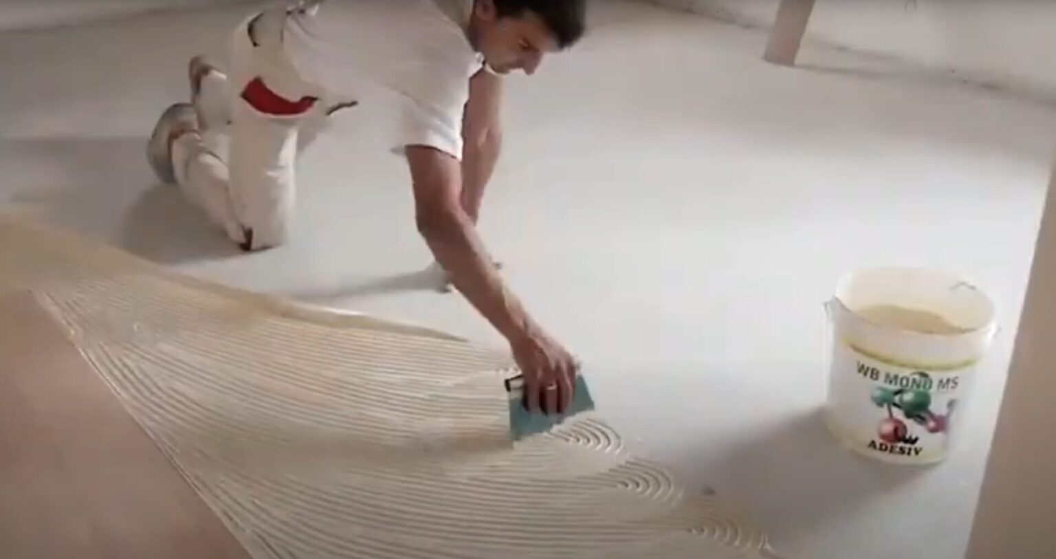 Installer spreading WB MONO MS Performance Plus wood floor adhesive evenly across a concrete subfloor using a notched trowel, preparing for glue-down hardwood installation in a residential home in Edmonton, Alberta